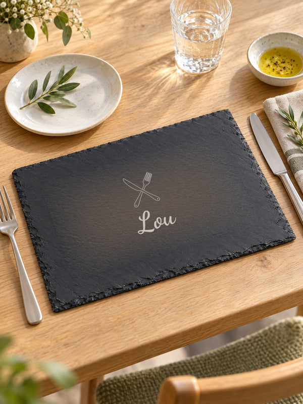 Visuel d’illustration – set de table en ardoise sur une table en bois clair avec une assiette et des couverts, gravé de couverts croisés et « Lou » (exemple)