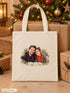 Visuel d’illustration – tote bag au pied d’un sapin de Noël, entre des paquets kraft, avec un portrait de couple fictif en style Portrait signature, prénoms « Camille & Hugo »