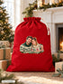 Visuel d’illustration – hotte de Noël rouge remplie de cadeaux près d’une cheminée décorée, avec le portrait d’un couple, style Noël douillet, texte « Camille & Hugo » en lettres dorées