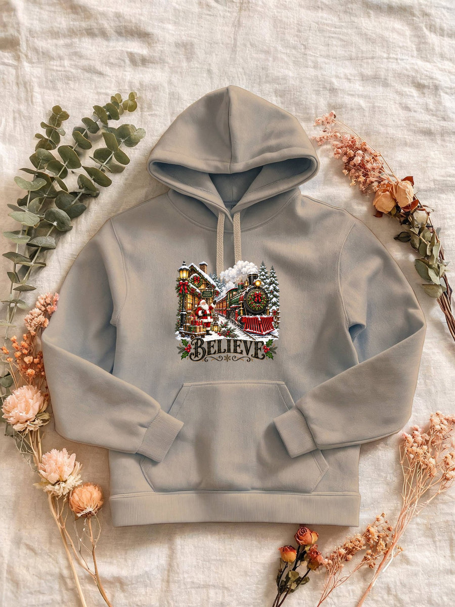Visuel d’illustration – Sweat femme sable avec le Père Noël et le train à vapeur devant la gare enneigée, « Believe »