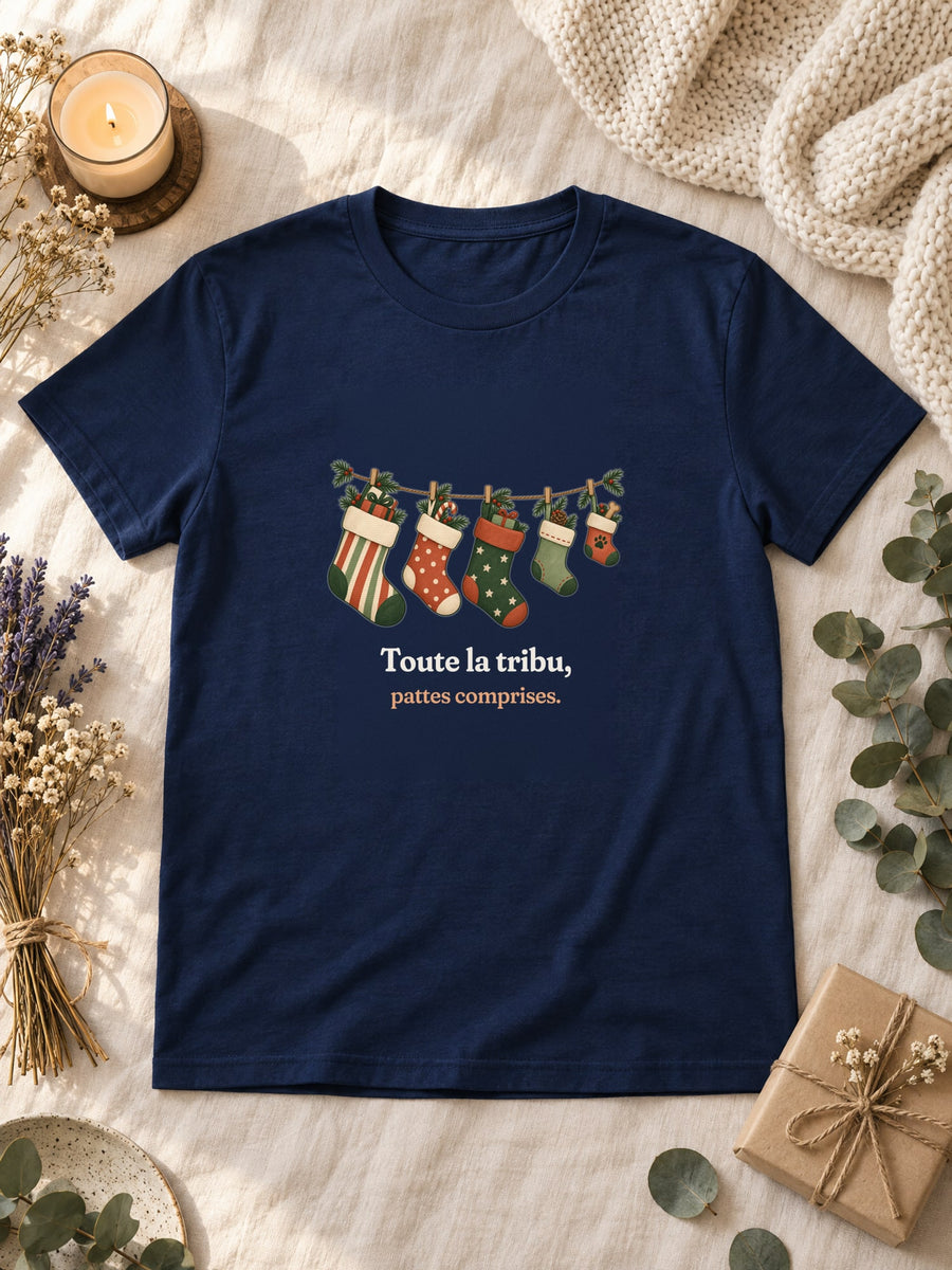 Visuel d’illustration – t-shirt navy posé à plat sur du lin, avec des fleurs séchées, une bougie et un paquet cadeau, avec le motif de Noël : une guirlande de chaussettes de Noël, dont une petite avec une empreinte de patte, et la phrase « Toute la tribu, pattes comprises. »