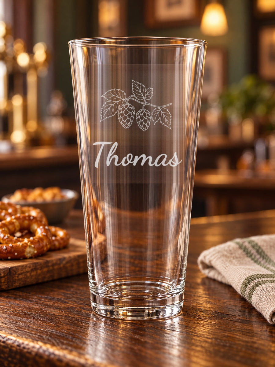 Visuel d’illustration – verre à bière sur un comptoir en chêne foncé, gravé d’un brin de houblon et « Thomas » (exemple)