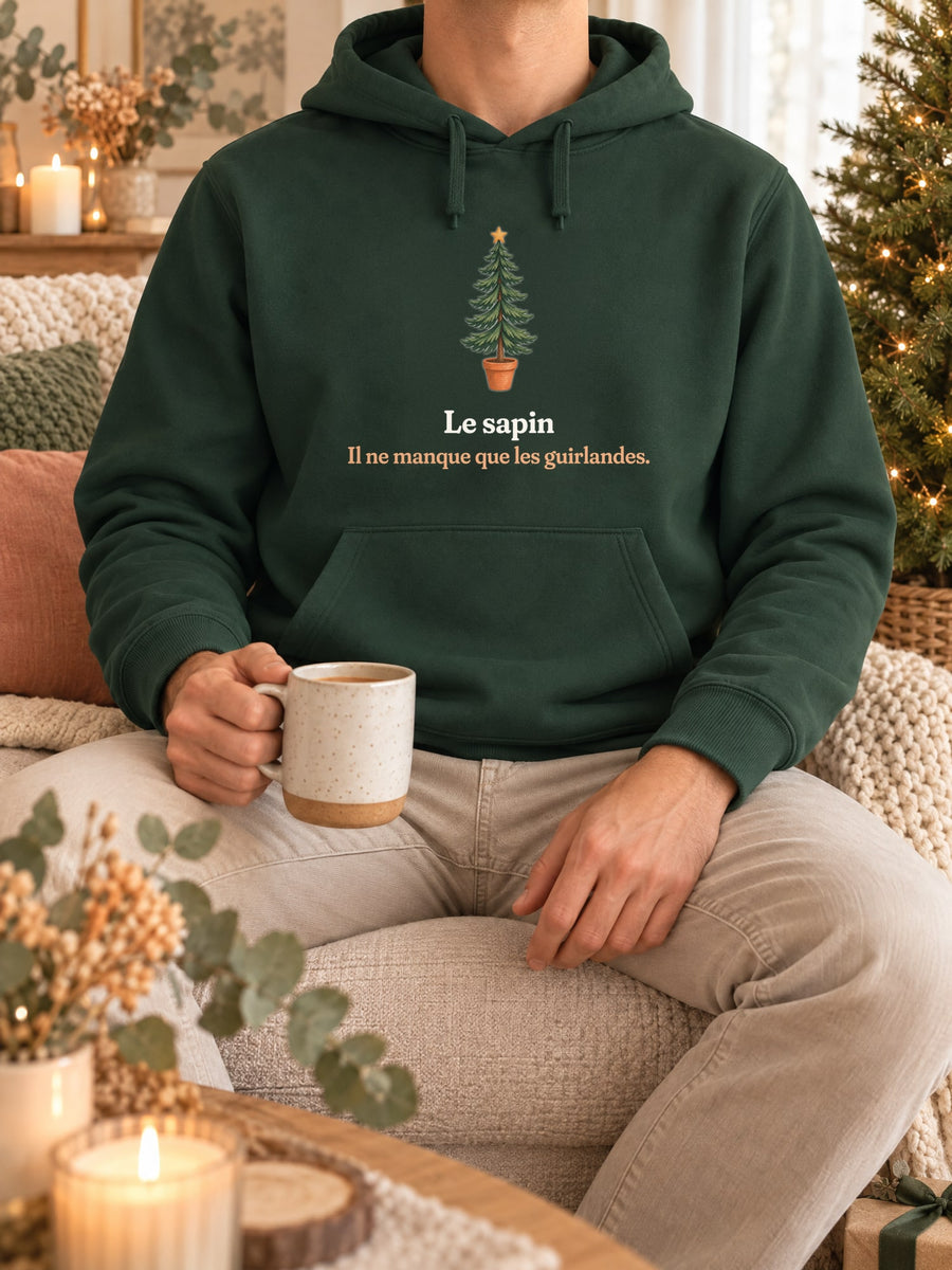 Visuel d’illustration – sweat à capuche vert forêt dans une mise en situation, avec le motif un sapin nu en pot et « Le sapin. Il ne manque que les guirlandes. »