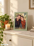 Visuel d’illustration – cadre vert pastel 21 × 30 cm posé sur une commode crème, à côté d’une plante et d’une bougie, avec un portrait de couple fictif, style plein cadre Peinture