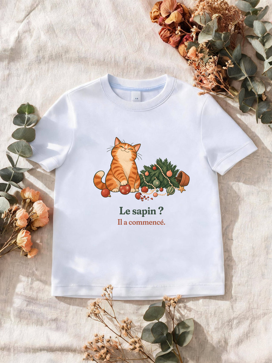 Visuel d’illustration – T-shirt homme blanc avec le motif de Noël : un chat roux assis près d’un sapin de Noël renversé et la phrase « Le sapin ? Il a commencé. »