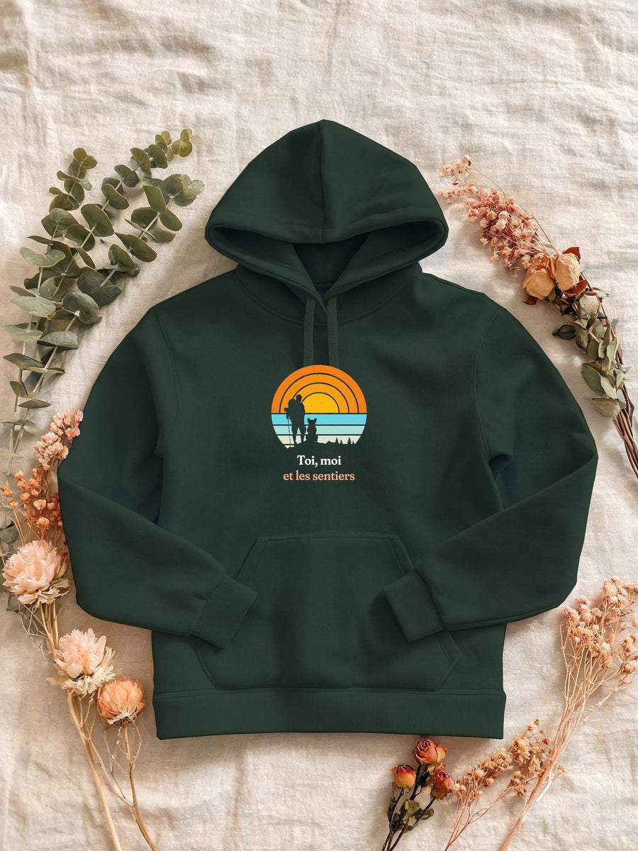 Visuel d’illustration – Sweat femme vert forêt avec le motif un randonneur et son chien assis, en silhouettes devant un grand soleil orange à bandes rétro et « Toi, moi et les sentiers »