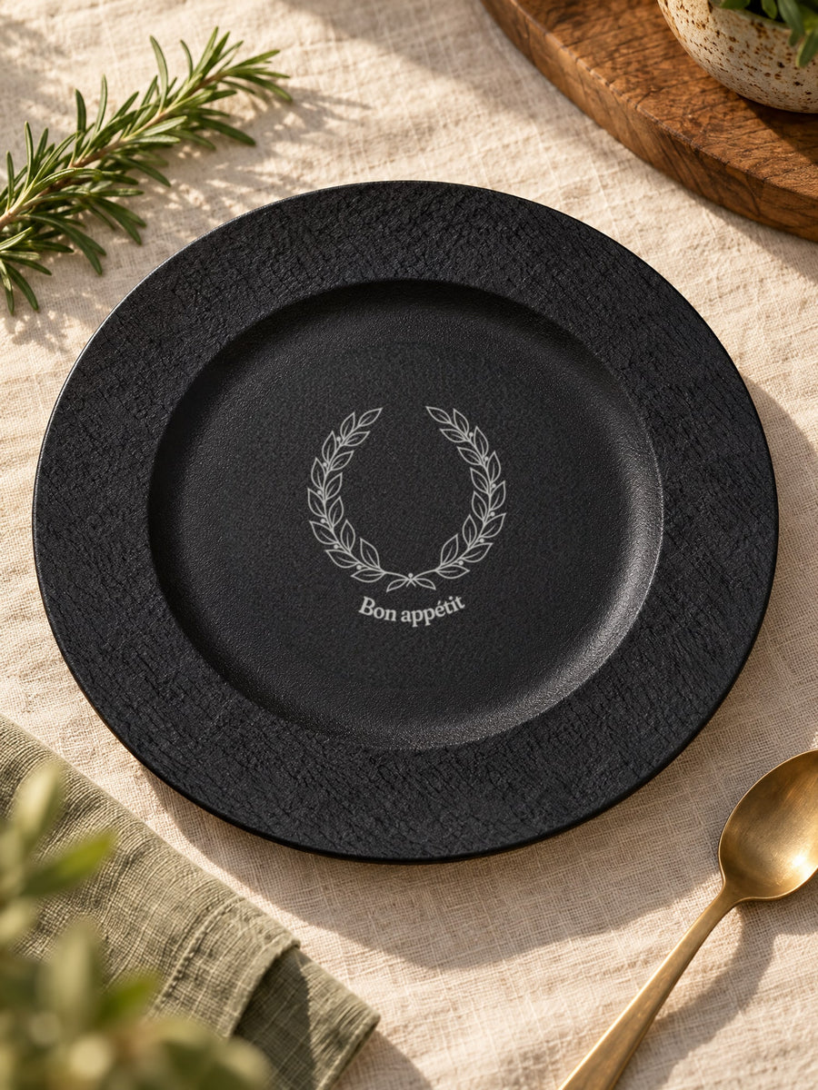 Visuel d’illustration – assiette noire posée sur une nappe en lin, gravée « Bon appétit » (exemple)