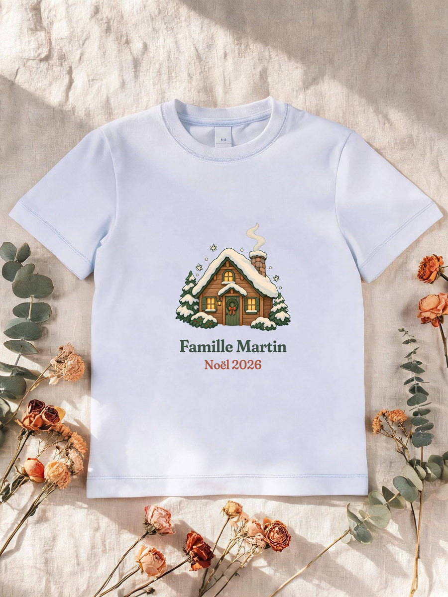 Visuel d’illustration – T-shirt enfant blanc avec le motif un chalet sous la neige et « Famille Martin · Noël 2026 » (exemple de nom)