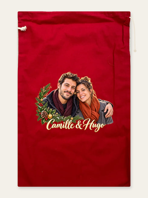 Visuel d’illustration – hotte de Noël en coton rouge cerise, 40 × 62 cm, à plat, vue de face, avec le portrait d’un couple, style Couronne de Noël, texte « Camille & Hugo » en lettres dorées