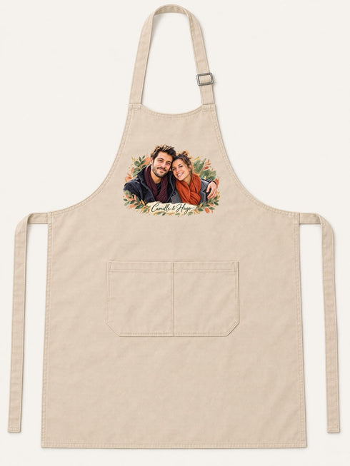 Visuel d’illustration – tablier de cuisine crème en coton, à plat, vue de face, avec un portrait de couple fictif en style Portrait signature, prénoms « Camille & Hugo »