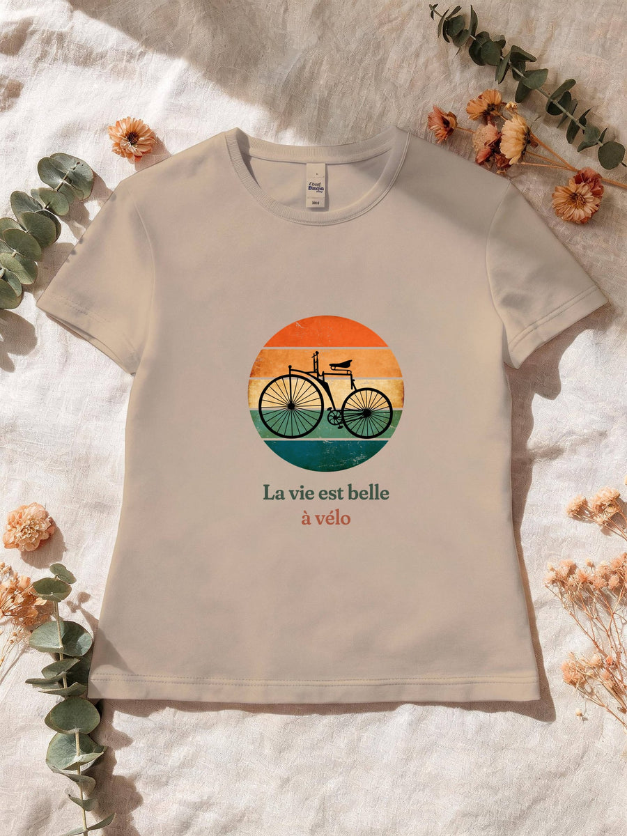 Visuel d’illustration – T-shirt femme sable avec le motif un vélo ancien à grande roue, en silhouette devant un soleil couchant à bandes rétro et « La vie est belle à vélo »