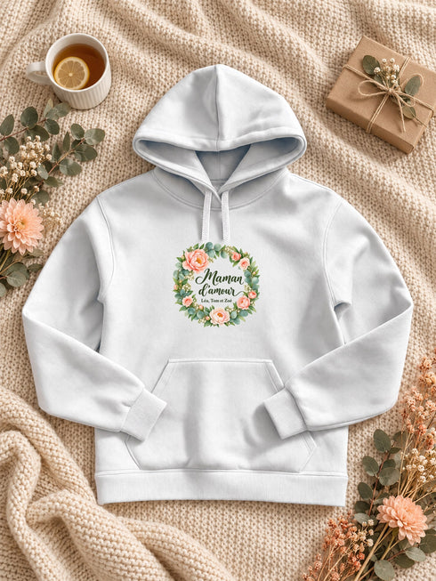 Visuel d’illustration – Sweat à capuche blanc avec le design « Maman d’amour », posé à plat sur un plaid, avec les prénoms d’exemple