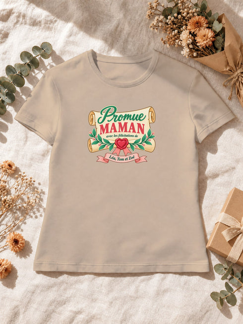Visuel d’illustration – T-shirt femme sable avec le design « Promue Maman », posé à plat avec des fleurs séchées, avec les prénoms d’exemple