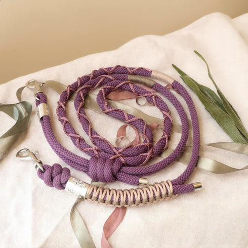 Cordon téléphonique artisanal tressé mauve et rose poudré avec mousquetons argentés, posé sur tissu beige