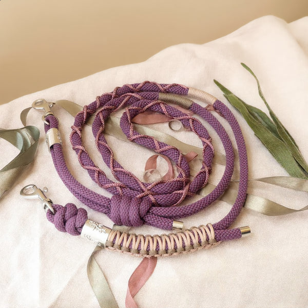 Cordon téléphonique artisanal tressé mauve et rose poudré avec mousquetons argentés, posé sur tissu beige