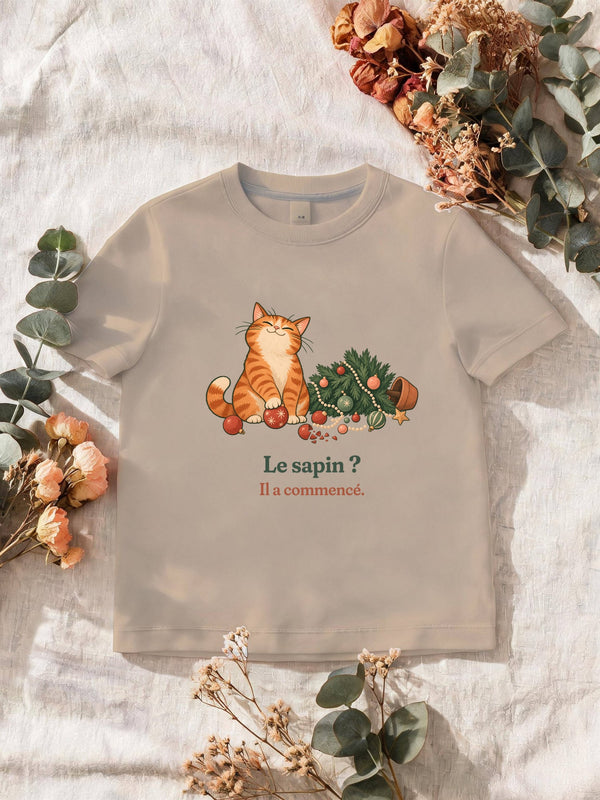 Visuel d’illustration – T-shirt homme sable avec le motif de Noël : un chat roux assis près d’un sapin de Noël renversé et la phrase « Le sapin ? Il a commencé. »