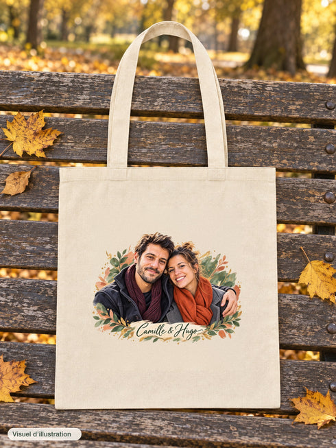 Visuel d’illustration – tote bag posé sur un banc en bois dans un parc en automne, avec un portrait de couple fictif en style Portrait signature, prénoms « Camille & Hugo »