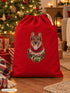 Visuel d’illustration – hotte de Noël rouge remplie de cadeaux au pied d’un sapin illuminé, avec le portrait de Caisy, un berger allemand, style Noël douillet, prénom en lettres dorées