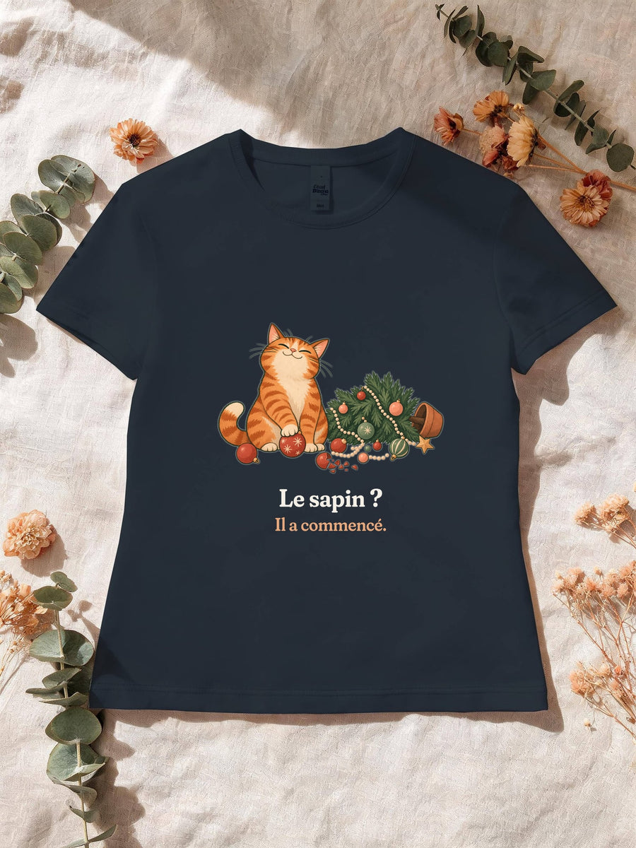 Visuel d’illustration – T-shirt femme navy avec le motif de Noël : un chat roux assis près d’un sapin de Noël renversé et la phrase « Le sapin ? Il a commencé. »