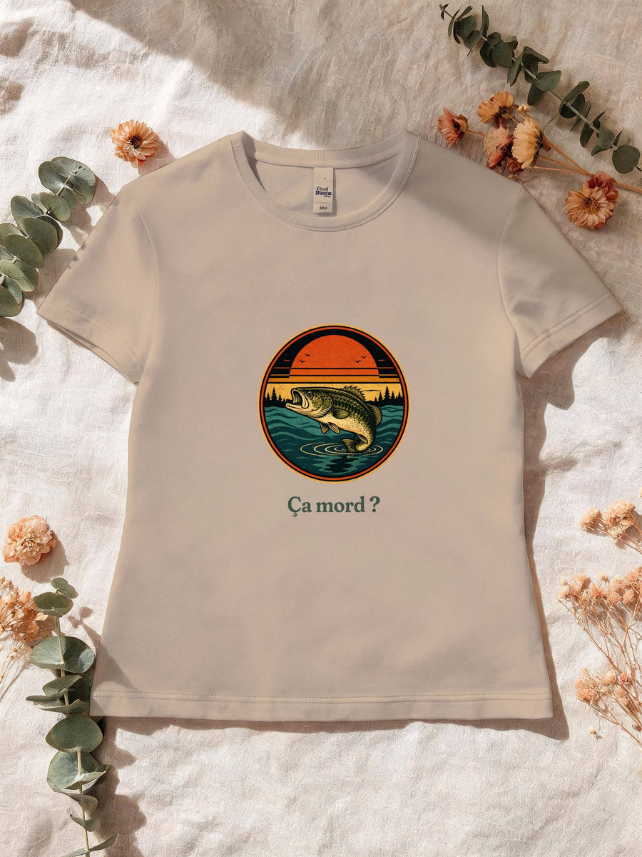 Visuel d’illustration – T-shirt femme sable avec le motif un poisson qui saute hors de l’eau devant un soleil couchant et des sapins, dans un médaillon rond et « Ça mord ? »