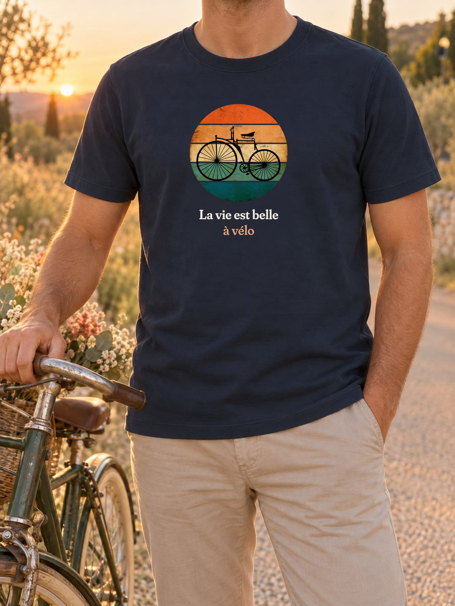 Visuel d’illustration – t-shirt dans une mise en situation, avec le motif un vélo ancien à grande roue, en silhouette devant un soleil couchant à bandes rétro et « La vie est belle à vélo »