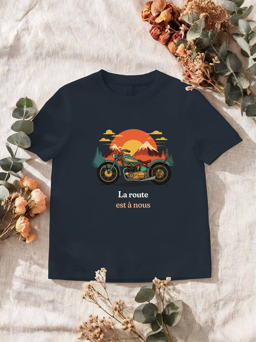 Visuel d’illustration – T-shirt homme navy avec le motif une moto ancienne illustrée en couleurs devant des montagnes, des sapins et un soleil couchant et « La route est à nous »