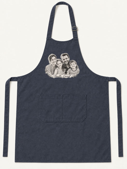 Visuel d’illustration – tablier de cuisine bleu marine en coton, à plat, vue de face, avec un portrait de famille fictive au crayon clair, style Croquis, texte « Famille Laurent »