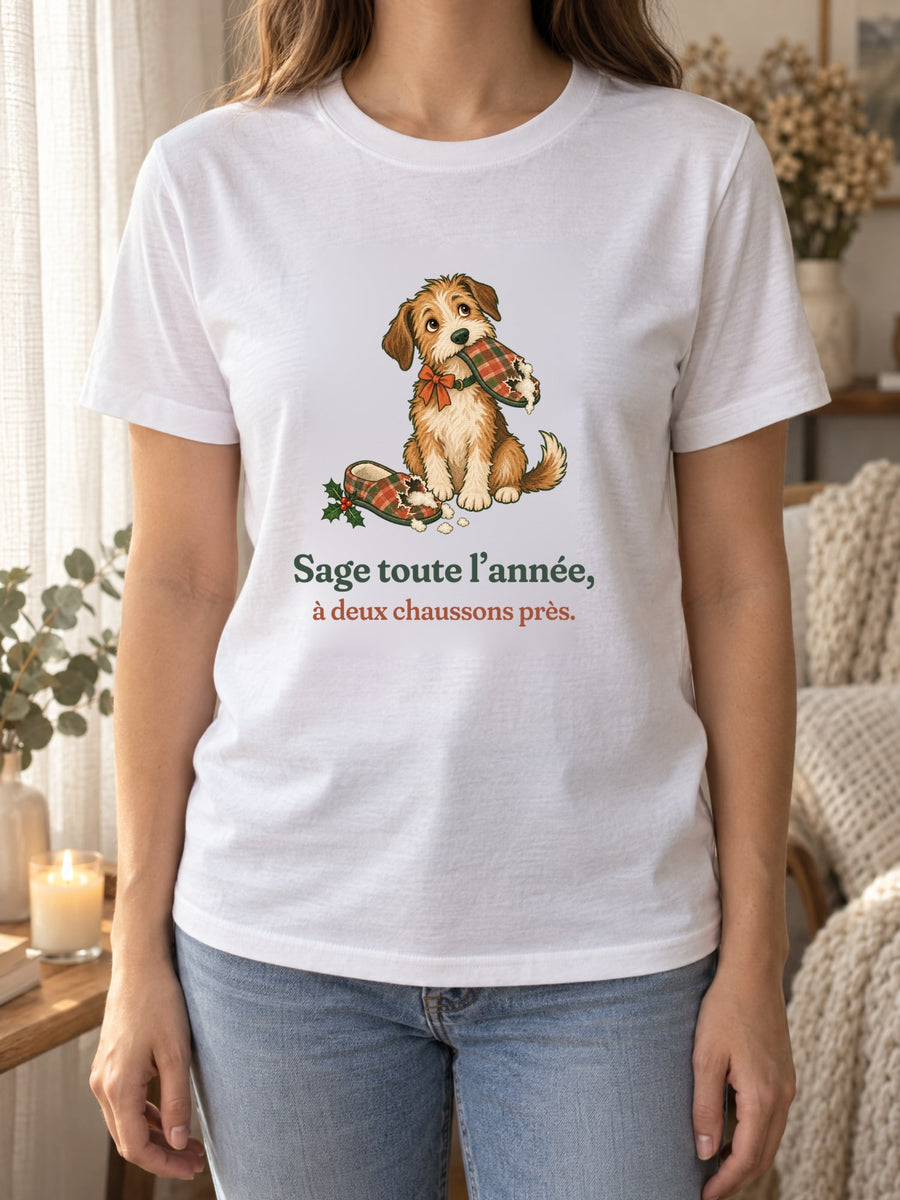 Visuel d’illustration – t-shirt blanc porté, près d’un rideau de lin et d’une bougie, avec le motif de Noël : un chien assis, un chausson dans la gueule, et la phrase « Sage toute l’année, à deux chaussons près. »