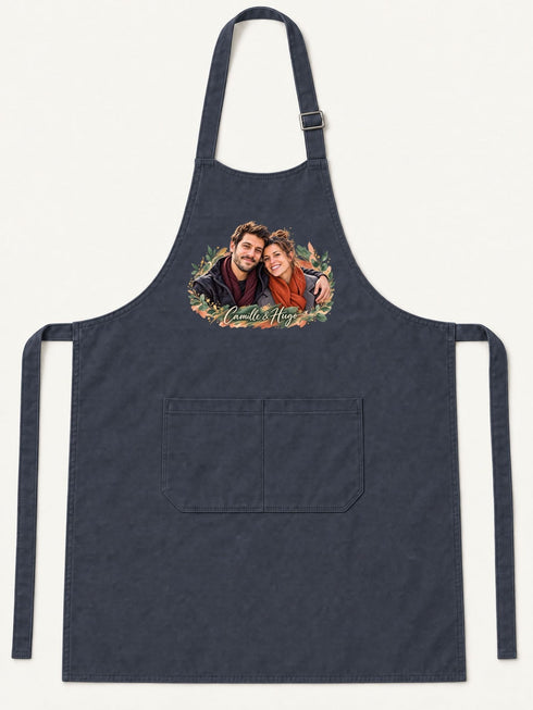 Visuel d’illustration – tablier de cuisine bleu marine en coton, à plat, vue de face, avec un portrait de couple fictif en style Portrait signature, prénoms clairs « Camille & Hugo »