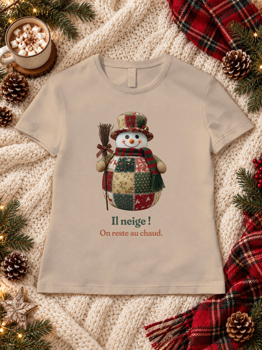Visuel d’illustration – t-shirt sable dans une mise en situation, avec le motif un bonhomme de neige en patchwork et « Il neige ! » et « On reste au chaud. »