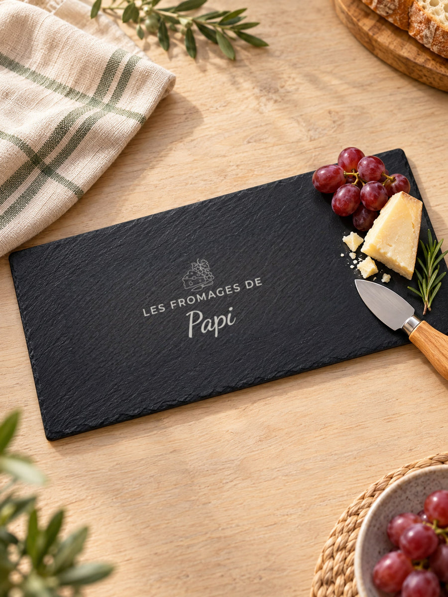 Visuel d’illustration – plateau en ardoise sur une table en bois clair avec un morceau de fromage et des raisins, gravé « Les fromages de Papi » (exemple)
