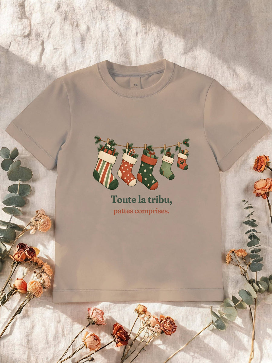 Visuel d’illustration – T-shirt enfant sable avec le motif de Noël : une guirlande de chaussettes de Noël, dont une petite avec une empreinte de patte, et la phrase « Toute la tribu, pattes comprises. »