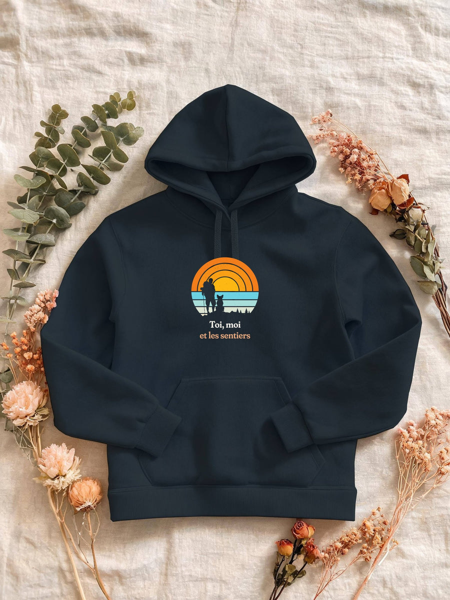 Visuel d’illustration – Sweat femme navy avec le motif un randonneur et son chien assis, en silhouettes devant un grand soleil orange à bandes rétro et « Toi, moi et les sentiers »