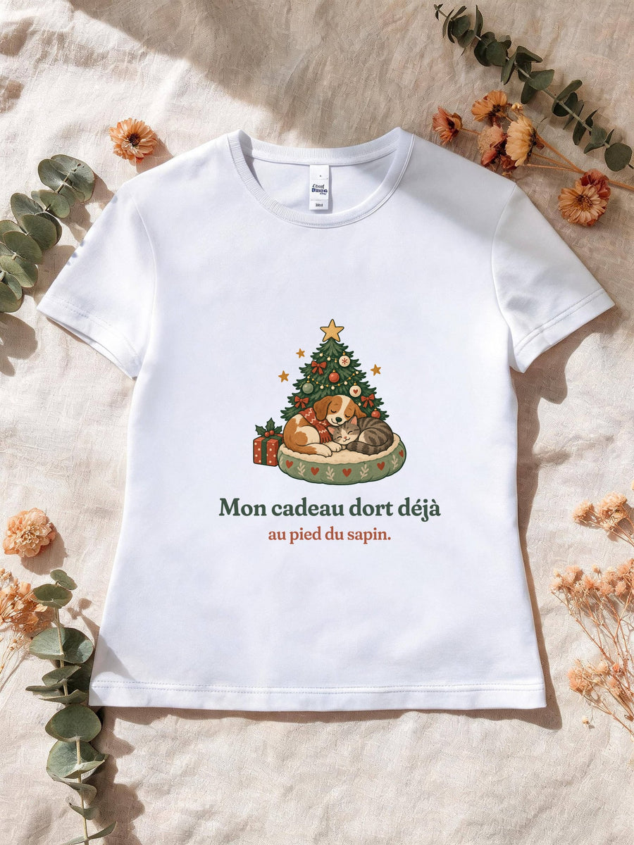Visuel d’illustration – T-shirt femme blanc avec le motif de Noël : un chien et un chat endormis au pied d’un petit sapin et la phrase « Mon cadeau dort déjà au pied du sapin. »