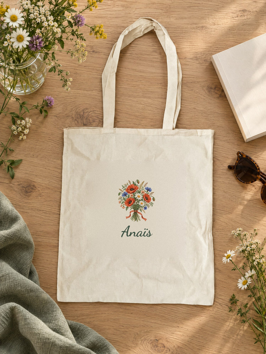 Visuel d’illustration – tote bag posé sur une table en chêne avec des fleurs, avec le bouquet et « Anaïs » (exemple de prénom)