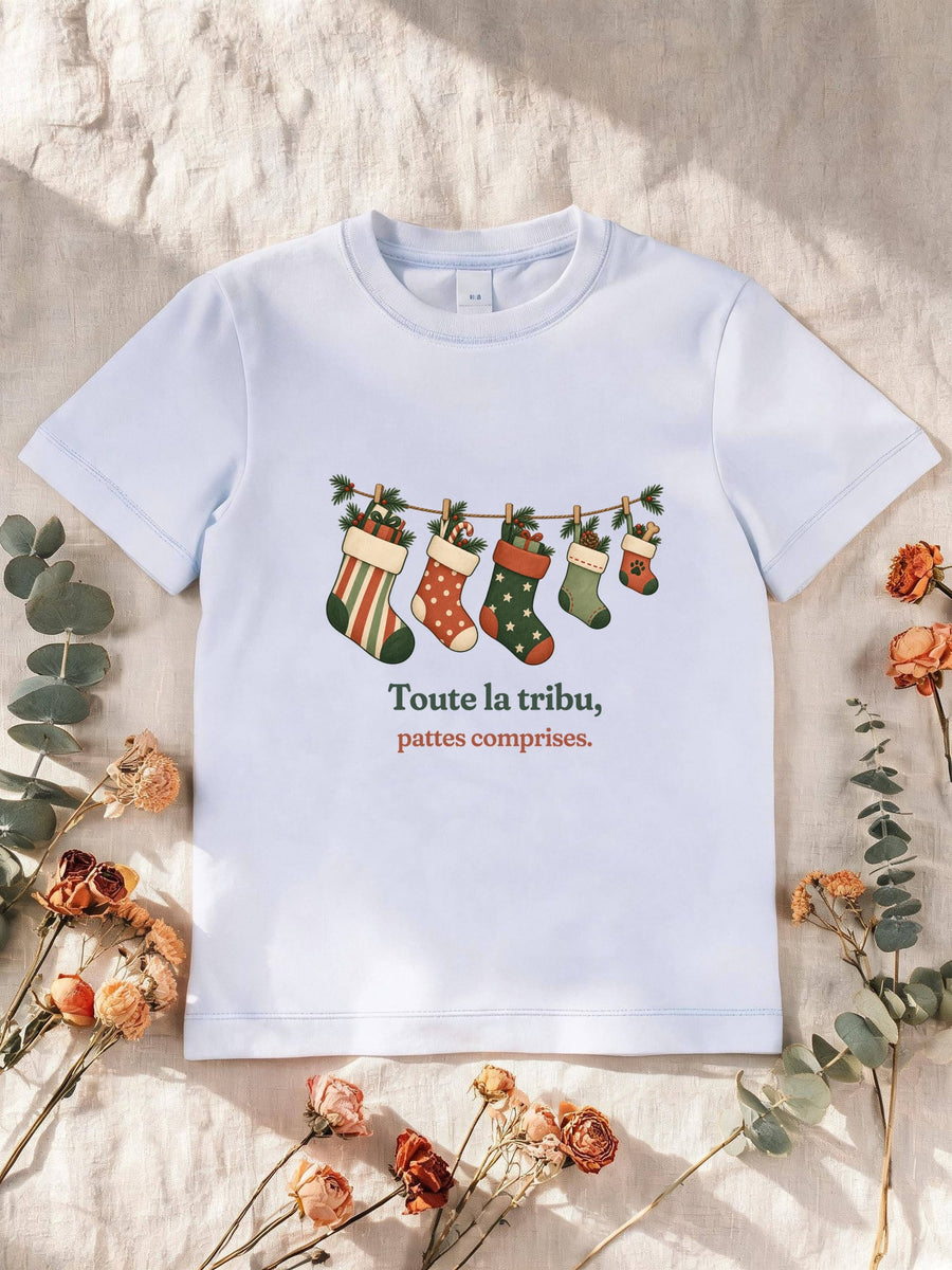 Visuel d’illustration – T-shirt enfant blanc avec le motif de Noël : une guirlande de chaussettes de Noël, dont une petite avec une empreinte de patte, et la phrase « Toute la tribu, pattes comprises. »