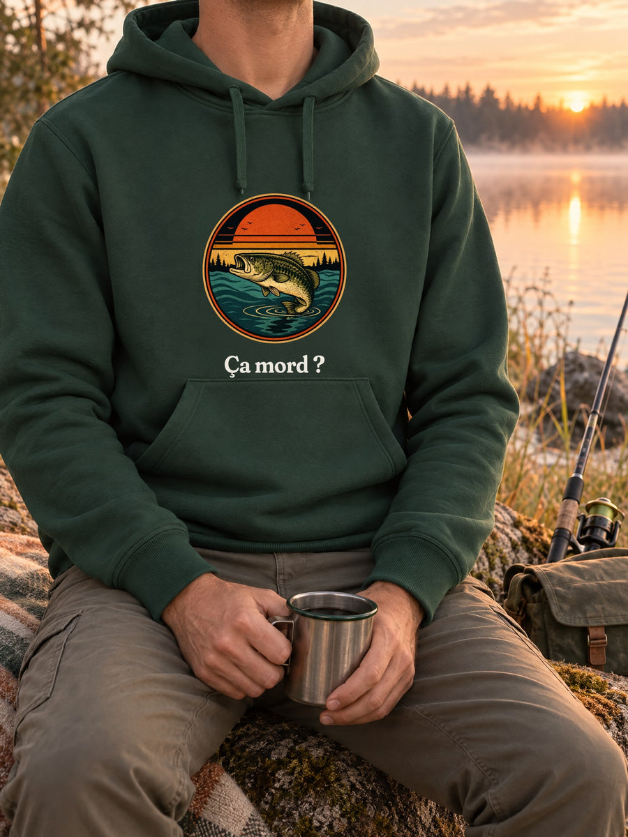 Visuel d’illustration – t-shirt dans une mise en situation, avec le motif un poisson qui saute hors de l’eau devant un soleil couchant et des sapins, dans un médaillon rond et « Ça mord ? »