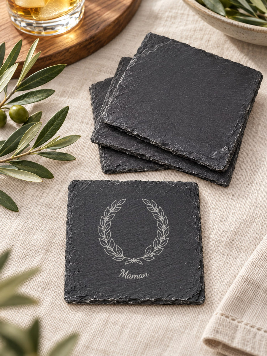 Visuel d’illustration – sous-verres en ardoise en éventail sur une nappe en lin, l’un gravé d’une couronne et de « Maman » en arc dessous (exemple)