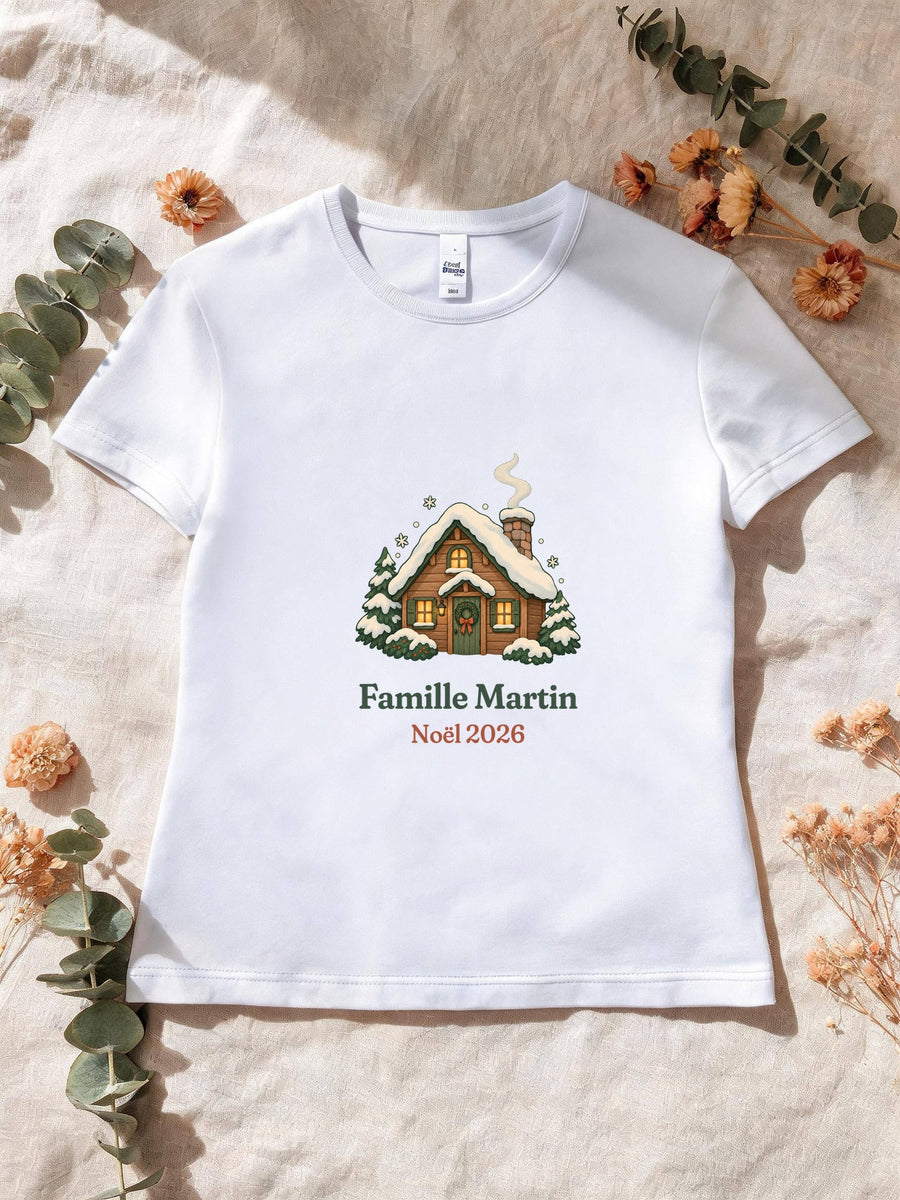 Visuel d’illustration – T-shirt femme blanc avec le motif un chalet sous la neige et « Famille Martin · Noël 2026 » (exemple de nom)