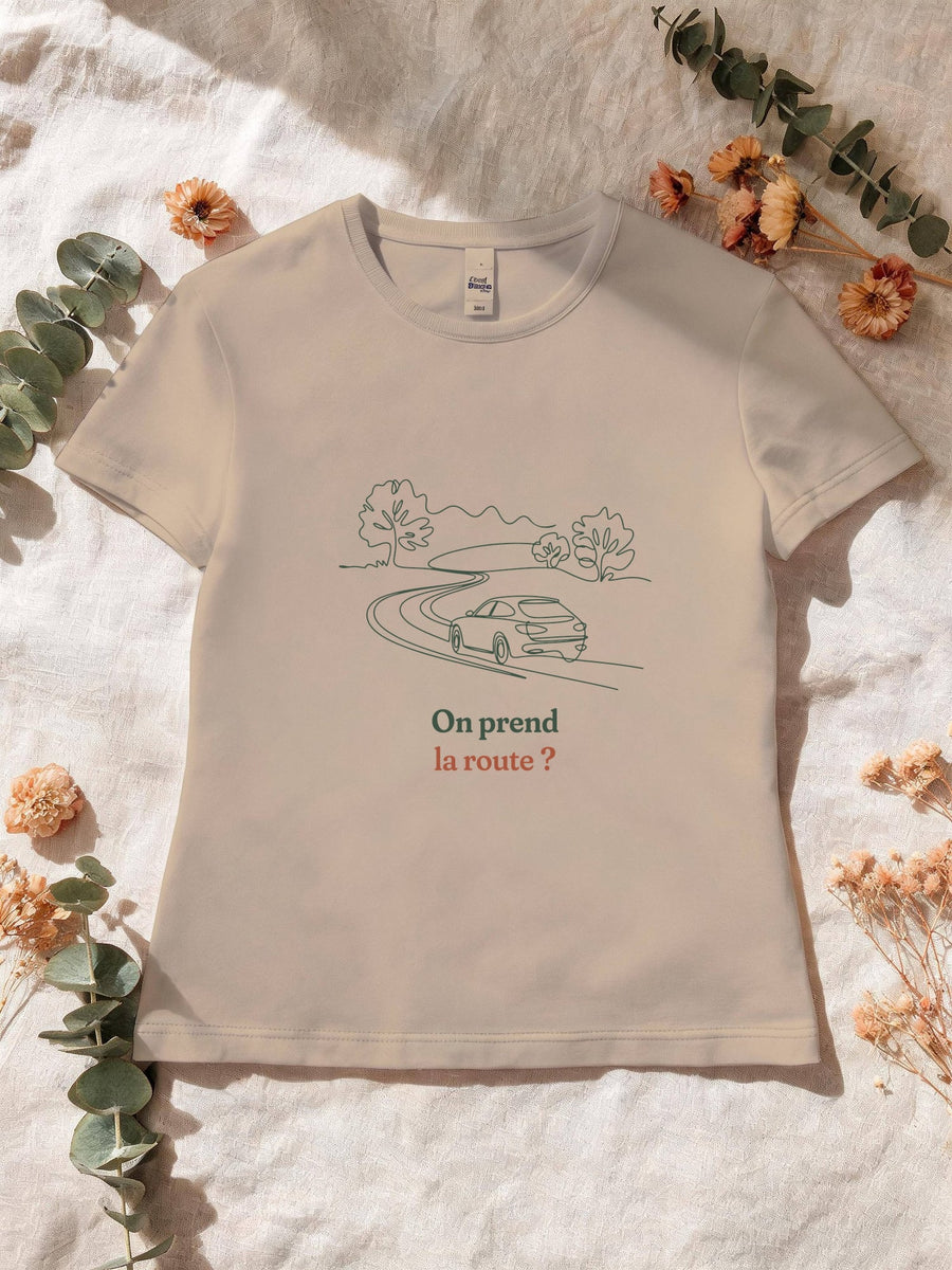 Visuel d’illustration – T-shirt femme sable avec le motif une voiture sur une route sinueuse entre les arbres, dessinée d’un seul trait continu et « On prend la route ? »