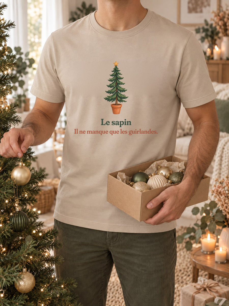 Visuel d’illustration – t-shirt sable dans une mise en situation, avec le motif un sapin nu en pot et « Le sapin. Il ne manque que les guirlandes. »