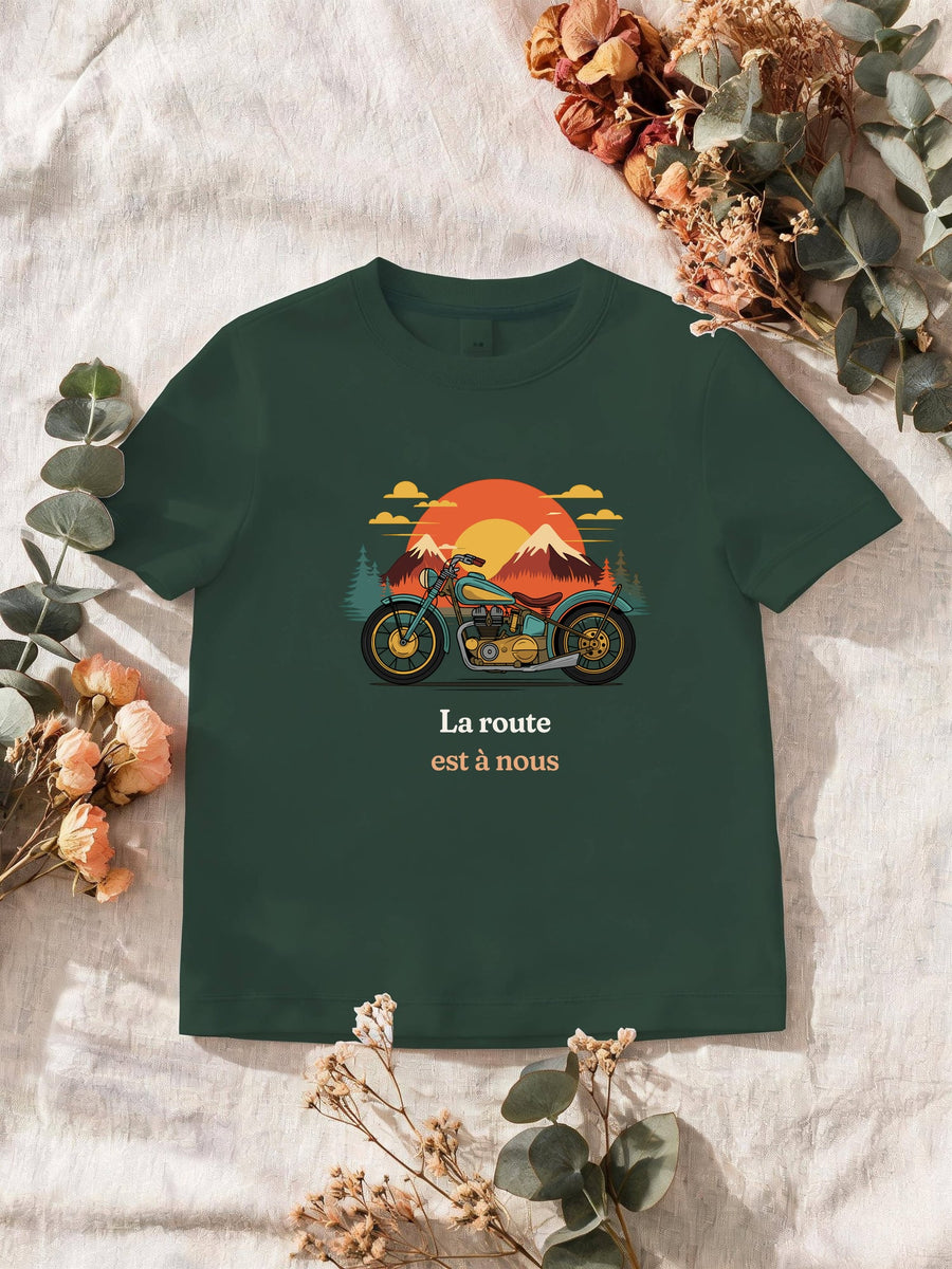 Visuel d’illustration – T-shirt homme vert forêt avec le motif une moto ancienne illustrée en couleurs devant des montagnes, des sapins et un soleil couchant et « La route est à nous »