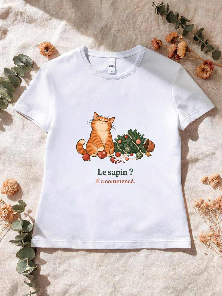 Visuel d’illustration – T-shirt femme blanc avec le motif de Noël : un chat roux assis près d’un sapin de Noël renversé et la phrase « Le sapin ? Il a commencé. »