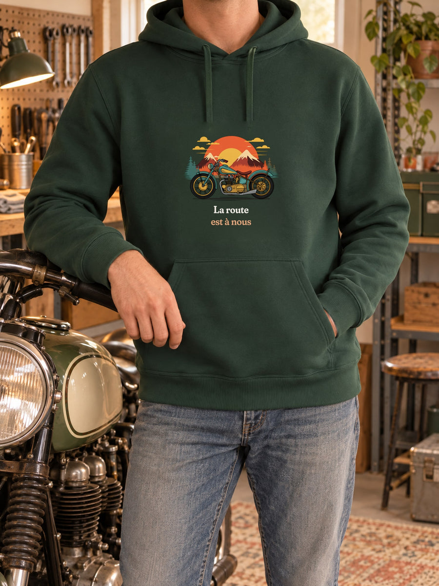 Visuel d’illustration – t-shirt dans une mise en situation, avec le motif une moto ancienne illustrée en couleurs devant des montagnes, des sapins et un soleil couchant et « La route est à nous »