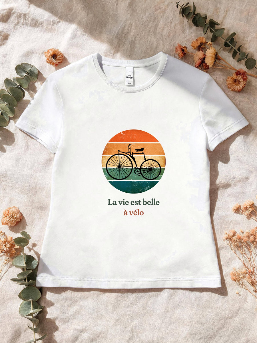 Visuel d’illustration – T-shirt femme blanc avec le motif un vélo ancien à grande roue, en silhouette devant un soleil couchant à bandes rétro et « La vie est belle à vélo »