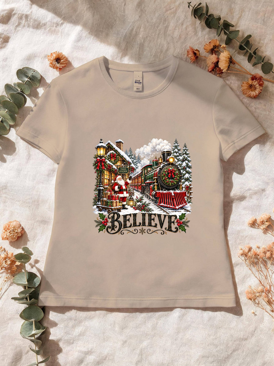 Visuel d’illustration – T-shirt femme sable avec le Père Noël et le train à vapeur devant la gare enneigée, « Believe »