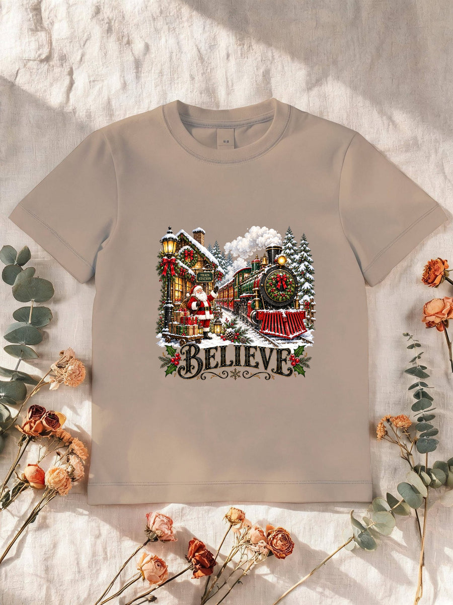 Visuel d’illustration – T-shirt enfant sable avec le Père Noël et le train à vapeur devant la gare enneigée, « Believe »