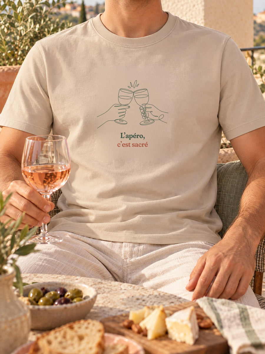 Visuel d’illustration – t-shirt dans une mise en situation, avec le motif deux mains qui trinquent avec deux verres à vin, dessinées d’un seul trait continu et « L’apéro, c’est sacré »