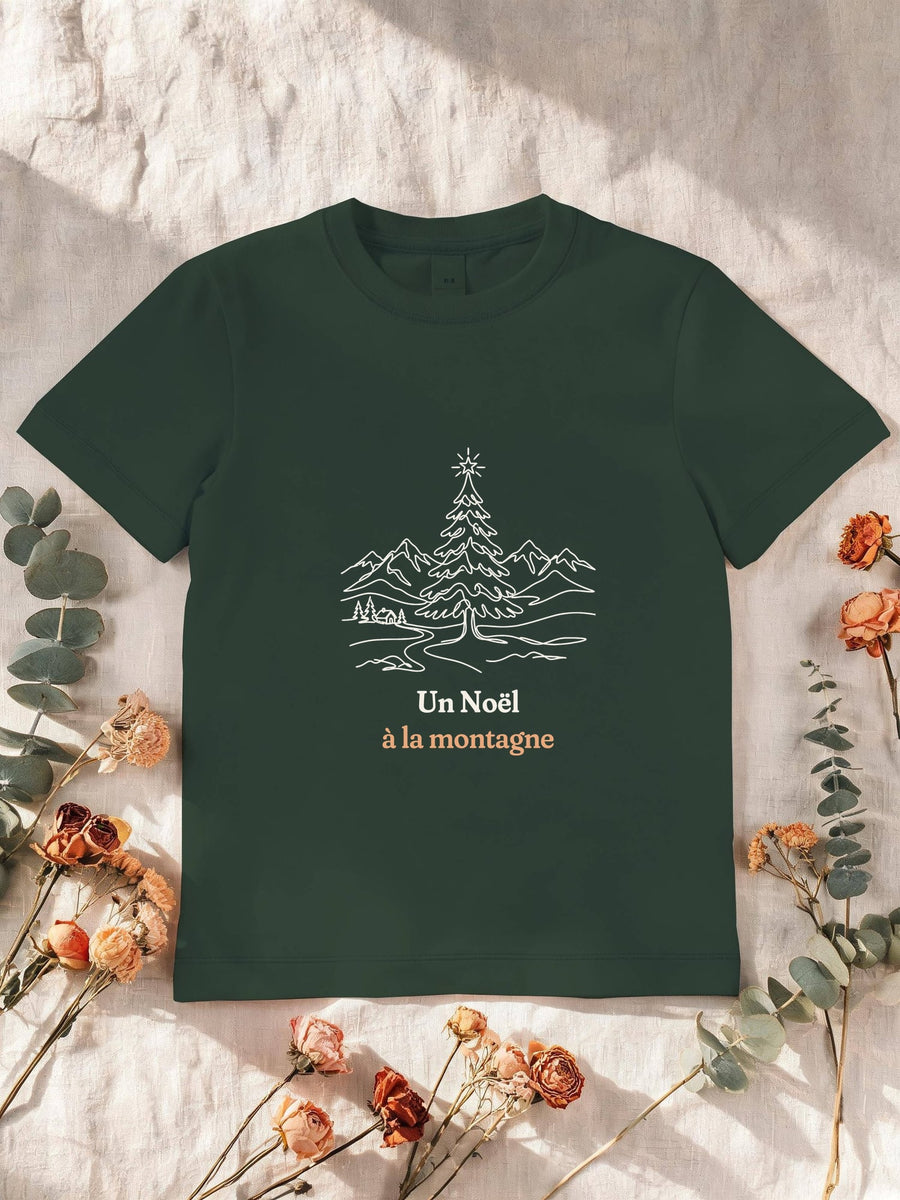 Visuel d’illustration – T-shirt enfant vert forêt avec le motif un sapin de Noël étoilé devant des montagnes enneigées, dessiné au trait et « Un Noël à la montagne »