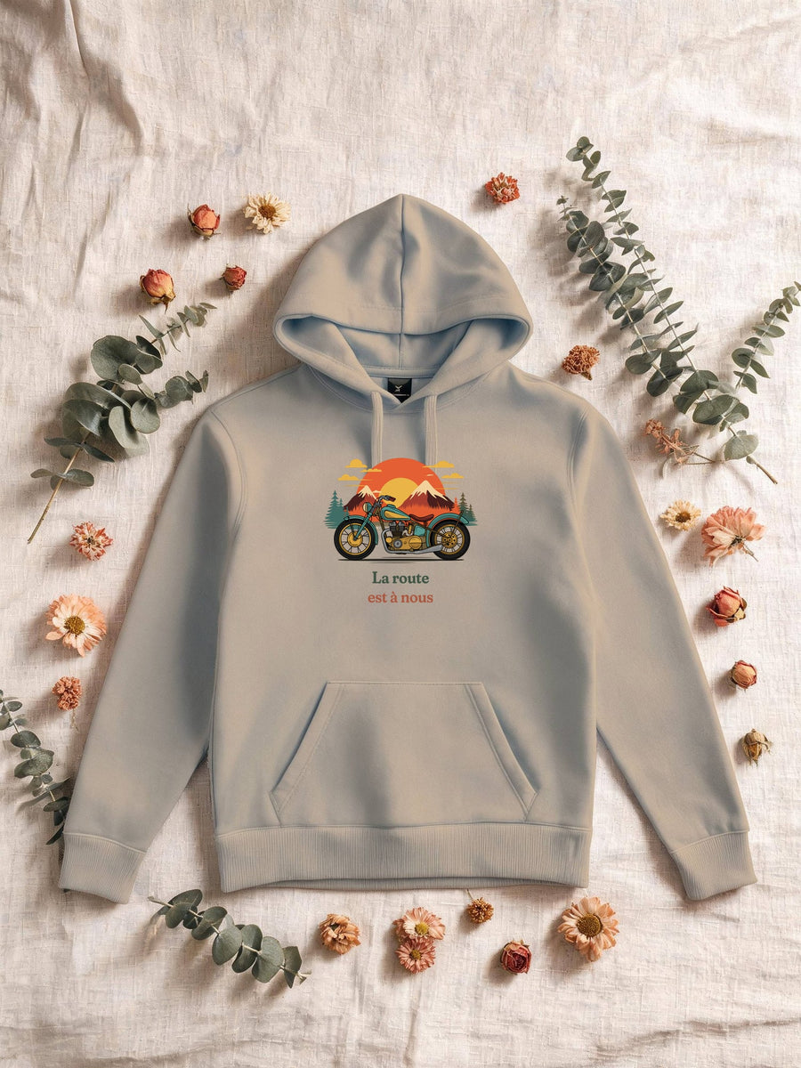 Visuel d’illustration – Sweat homme sable avec le motif une moto ancienne illustrée en couleurs devant des montagnes, des sapins et un soleil couchant et « La route est à nous »